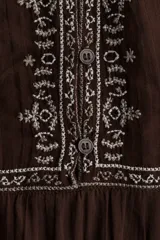 Blusa de algodón con textura arrugada, color marrón, con detalles bordados en contraste en el frente y las mangas. Presenta escote redondo, cierre frontal con botones, mangas globo largas y puños abotonados.