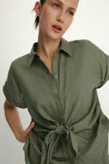 Camisa blanca confeccionada en tejido con lino, con cuello solapa y manga muy corta con terminación en vuelta. Presenta un detalle de nudo en el delantero y cierre frontal con botones metálicos.