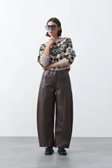 Pantalón de cuero sintético con fit barrel, de silueta amplia con volumen en las piernas y botamanga levemente entallada. Presenta bolsillos laterales y cierre frontal.