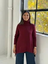 Sweater de punto color bordó con cuello alto tipo polera, diseño de corte evasé con costura central vertical y bajo asimétrico más largo en la parte posterior.