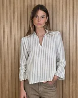 Blusa color lila con estampado vertical de ramas y hojas blancas, cuello alto con volados y escote en V. Presenta mangas largas abullonadas con puños elastizados.