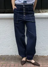 Jean 2 en 1 de color azul oscuro, con corte wide leg transformable a babucha mediante ajuste en los tobillos, tiro alto con cierre frontal de múltiples botones metálicos y bolsillos delanteros destacados.