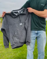 Buzo con medio cierre gris oscuro con efecto lavado stone wash, de corte oversized, mangas largas, cuello alto y bolsillo tipo canguro al frente con una pequeña etiqueta blanca con la marca.