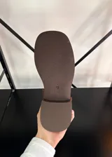 Bota tipo biker de caña media en cuero vegano color marrón, con suela track y múltiples correas con hebillas metálicas plateadas en el tobillo y la parte superior de la caña.