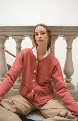 Cardigan de punto color beige con cuello redondo, cierre frontal con botones dorados, bolsillos frontales y terminaciones en crochet. Presenta hombreras internas y diseño de corte recto.