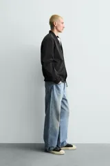 Cazadora bomber ligera de tejido técnico color verde oliva, con cuello, puños y bajo en rib elástico. Presenta cierre frontal de cremallera y bolsillos de vivo en la cadera.