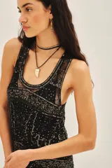 Vestido corto negro de calce recto, sin mangas y escote redondo. Confeccionado en tul bordado con piedras, lentejuelas, canutillos y flecos de mostacillas. Incluye un viso a tono con breteles finos.