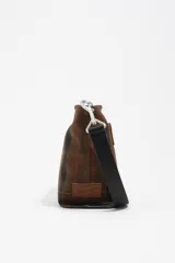 Bolso bandolera de gabardina con estampado de cuadros en tonos marrones y verdes, con asa de cinta negra regulable y logo de la marca estampado en la parte inferior.