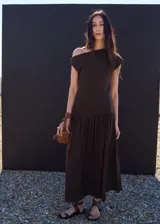 Vestido largo marrón de diseño asimétrico y corte evasé, con cuello barco y manga corta.