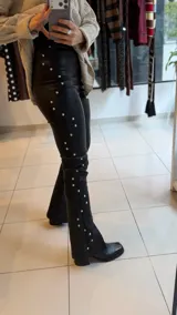 Pantalon de gabardina elastizada color negro, de corte ajustado con diseño de tachas metálicas plateadas a lo largo de las costuras laterales.