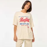 Remera color crudo de corte amplio con mangas cortas con dobladillo. Estampado frontal con la frase "Where Dreams Meet Reality New York BIG CITY LIFE EAST SIDE" en letras rojas y azules.