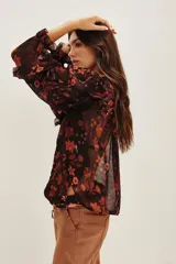 Camisa de viscosa con estampado floral en tonos rojizos y naranjas sobre fondo negro. Presenta volados en los hombros y mangas largas con terminaciones delicadas.