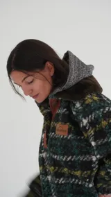 Buzo canguro oversize de paño de lana gris con capucha estampada y cuello de corderito blanco. Cuenta con aberturas laterales en el ruedo y detalles de cuero sintético marrón en el cierre frontal y etiqueta.