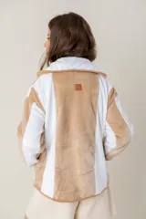 Campera de peluche con diseño de paneles verticales en colores blanco y beige. Presenta capucha, cierre frontal y puños de tejido elástico en tono contrastante.