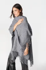 Ruana de tejido suave y envolvente en color blanco, con diseño de corte amplio y terminación de flecos en el ruedo.