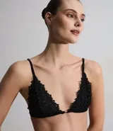 Soutien tipo bralette de encaje negro con diseño triangular, sin aros ni relleno. Cuenta con breteles finos ajustables y un pequeño detalle metálico en el centro del escote.