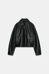 Cazadora corta negra de efecto piel, con cuello solapa, manga larga y cierre frontal con botones a presión ocultos. Incluye bolsillos delanteros de vivo con botón a presión y bajo con elástico en la espalda.