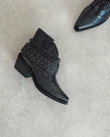 Botines cortos plateados de cuero vacuno, con punta fina, taco bajo y detalle de tachas y correas alrededor del tobillo.