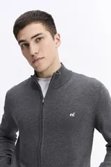 Campera tejida de algodón en color beige, con cierre frontal completo, cuello levemente elevado y puños y ruedo acanalados. Presenta un pequeño logo bordado en el pecho.