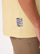 Remera de manga corta color amarillo, corte holgado, con gran estampado en la espalda de un perro en bicicleta con una tabla de surf y un loro, acompañado del texto "Wild by Nature Rusty Worldwide".