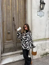 Buzo de peluche con estampado animal print en blanco y negro, de corte holgado, cuello alto y cierre frontal parcial con tirador metálico.