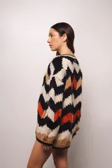 Buzo tejido a mano en lana merino, con diseño de patrón en zigzag multicolor en tonos crema, negro, azul y tostado. Presenta un corte holgado, cuello redondo y mangas largas con puños acanalados.