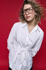 Camisa blanca de manga larga con volumen y estructura, cierre frontal con botones y lazo ajustable en la cintura que realza la silueta.