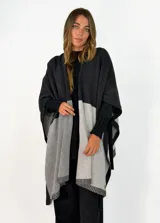 Ruana de tejido de punto con diseño color block en tonos gris oscuro, gris claro y negro, con terminaciones acanaladas en los bordes.