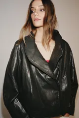Chaqueta de corte amplio estilo biker en tejido efecto piel de color verde oscuro, con cuello alto envolvente, cierre frontal asimétrico de cremallera metálica, bolsillos ocultos en costura y forro interior.