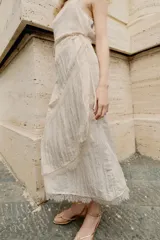 Vestido midi lencero de color blanco, confeccionado en tejido con efecto arrugado. Cuenta con escote recto, tirantes finos ajustables, diseño cruzado con cinturón fino para anudar y detalles de encaje en los acabados de la falda.