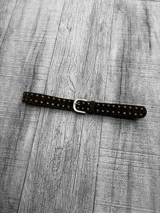 Cinto marrón de gamuza con tachas doradas y hebilla metálica plateada.