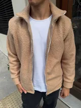 Campera de corderito color beige con cierre frontal completo y cuello alto. Presenta puños y ruedo acanalados, con detalles de terminación en tela lisa a lo largo del cierre.