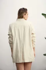 Blazer de mujer color rosa pálido, de corte recto y largo, con solapas de muesca y un solo botón frontal marrón. Presenta bolsillos de parche en la parte delantera y mangas tres cuartos.