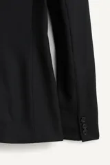 Blazer negro de corte recto de la colección Zara Studio, con solapas de muesca, cierre frontal de dos botones y bolsillos con solapa. Presenta mangas largas con pliegues estructurados en los hombros y forro interior a rayas a contraste.