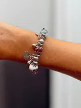 Pulsera rígida plateada con dijes colgantes y cuentas decorativas. Incluye cuentas de cristal facetado, cuentas de cerámica con estampado floral, cuentas de piedra veteada y dijes metálicos con forma de corazón, hoja y gota.