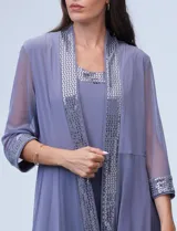 Conjunto de fiesta marca RM Richards, compuesto por vestido corto azul marino de seda fría con apliques bordados y chaqueta de seda fría con apliques bordados y mangas de microtul. El vestido tiene corte recto y largo a la rodilla. La chaqueta es abierta, con mangas 3/4 y largo a la cadera. El conjunto tiene forro interno a tono.