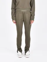 Pantalon deportivo color verde oliva, de corte ajustado con costuras frontales verticales y cierre en los tobillos. Cuenta con cintura elástica con cordón ajustable.