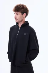 Buzo de felpa color negro con cuello alto y cierre frontal parcial. Presenta un diseño holgado con bolsillos laterales y logo bordado en el pecho.