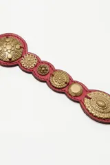 Cinturón de cuero rojo con apliques metálicos circulares y ovalados grabados a lo largo de toda la tira.