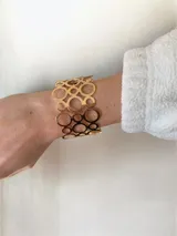 Brazalete ancho de diseño calado con formas circulares entrelazadas de diferentes tamaños, acabado en tono dorado brillante.