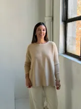 Sweater de punto en color beige, con cuello redondo, mangas largas con puños ajustados y diseño holgado con aberturas laterales en el ruedo.