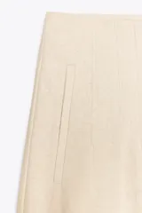 Pantalón de lino negro, de tiro alto, con bolsillos delanteros de vivo, pernera recta y cierre frontal con cremallera, botón interior y gancho metálico.