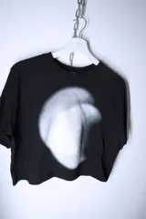 Remera negra de corte holgado y diseño cropped, con estampado frontal abstracto en tonos blancos y grises que simula un efecto de luz difusa.