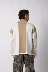 Sweater de tejido de punto con diseño de rayas verticales en tonos beige y blanco. Presenta cuello polo abierto, mangas largas y un corte holgado. Incluye un logo bordado en el centro del pecho.