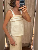 Top de lino color blanco de silueta relajada con tirantes anchos y detalles de puntilla y cintas bordadas en el frente.