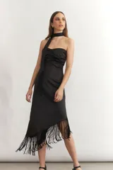 Vestido midi negro, sin mangas, con escote strapless fruncido y un detalle de tira ancha que se ata al cuello como un choker. La falda es asimétrica y termina con flecos largos.