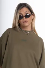 Remerón de jersey pesado color verde oliva, con cuello redondo y manga corta. Presenta un estampado sutil en el pecho y un estampado más grande en la espalda.