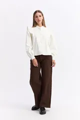 Camisa de color bordó con cuello mao y cierre frontal de botones. Presenta volados en los hombros que aportan volumen y un diseño sofisticado.