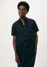 Camisa de manga corta con cuello clásico, cierre frontal de botones y bolsillo en el pecho.