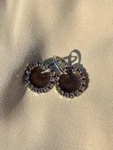 Aros colgantes con forma circular, hechos de resina color lila y borde de strass plateado. El aro es de acero quirúrgico plateado.